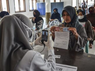 Petugas memotret identitas penerima bantuan sebagai tanda bukti saat penyaluran bantuan sosial (bansos) di Kantor Desa Sindangherang, Kabupaten Ciamis, Jawa Barat. Foto: Antara foto/ Adeng Bustomi