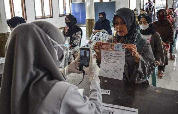 Petugas memotret identitas penerima bantuan sebagai tanda bukti saat penyaluran bantuan sosial (bansos) di Kantor Desa Sindangherang, Kabupaten Ciamis, Jawa Barat. Foto: Antara foto/ Adeng Bustomi